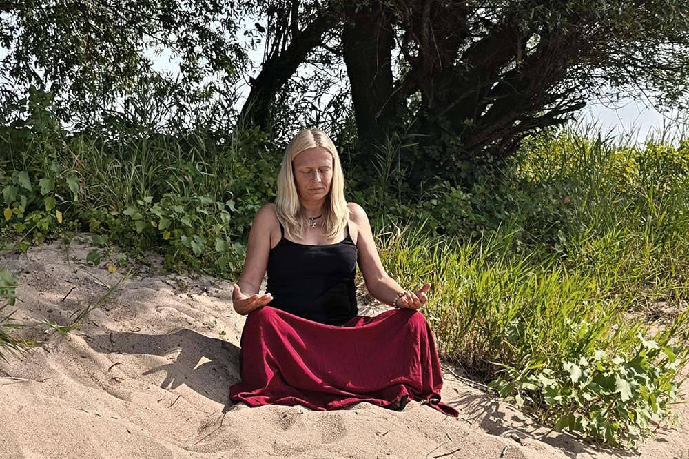 Person meditiert am Ufer der Elbe, im Hintergrund ein Baum